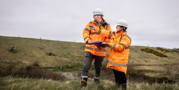 Two employees from Egniol in hi-vis jackets and hard hats survey the landfill site